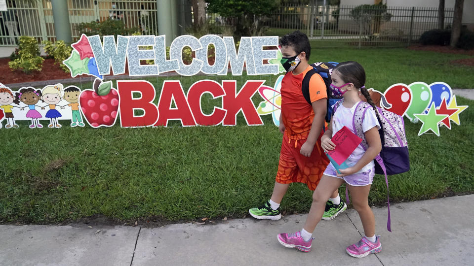 FILE - In this Tuesday, Aug. 10, 2021 file photo, Students wearing protective masks walk past a "Welcome Back" sign before the first day of school at Sessums Elementary School in Riverview, Fla. Students are required to wear the masks at school unless their parents opt out. President Joe Biden has called school district superintendents in Florida and Arizona, praising them for doing what he called “the right thing” after their respective boards implemented mask requirements in defiance of their Republican governors amid growing COVID-19 infections. (AP Photo/Chris O'Meara, File)