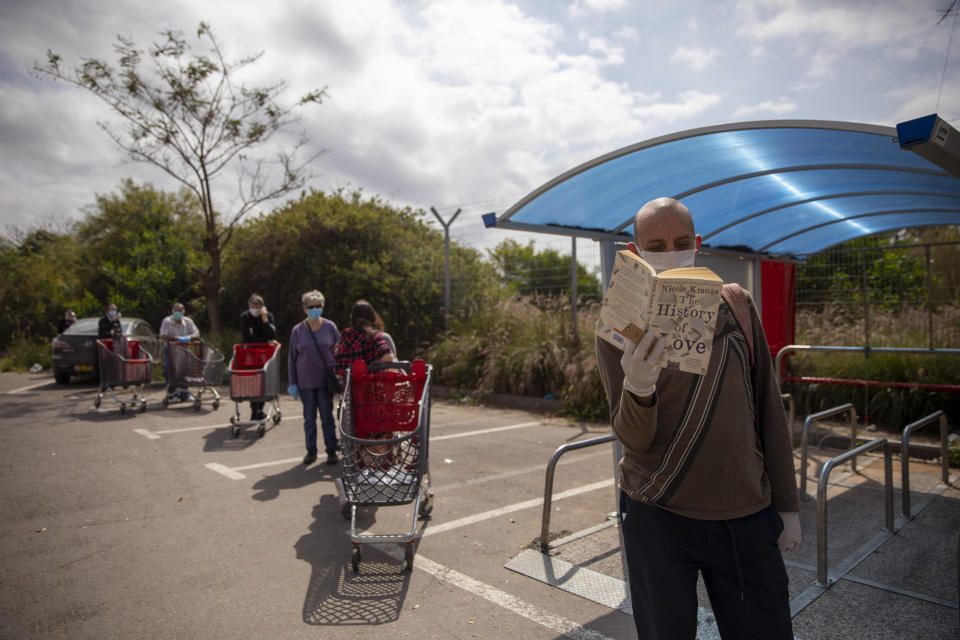 A customer reads a book as he and others line up to enter a supermarket keeping social distancing, following the government's measures to help stop the spread of the coronavirus, in Tel Aviv, Israel, Tuesday, April 7, 2020. Israeli Prime Minister Benjamin Netanyahu announced Monday a complete lockdown over the upcoming Passover holiday to control the country's coronavirus outbreak, but offered citizens some hope by saying he expects to lift widespread restrictions after the week-long festival. (AP Photo/Oded Balilty)