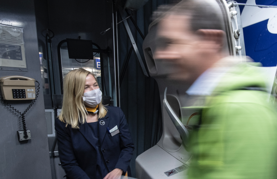 A flight attendant with a face mask welcomes passengers of a Boeing 747 of Lufthansa after landing at Frankfurt Airport. (Photo: Boris Roessler/picture alliance via Getty Images)