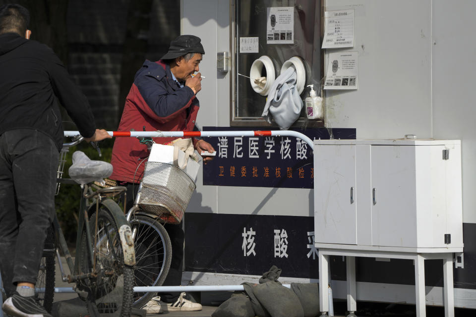 A man holds a cigarette as he preparing to get his routine COVID-19 throat swab at a coronavirus testing site setup outside the Drum Tower in Beijing, Tuesday, Nov. 1, 2022. Visitors to Shanghai Disneyland were temporarily blocked from leaving as part of virus testing that extended to more than 400,000 people, the city government announced Tuesday. (AP Photo/Andy Wong)