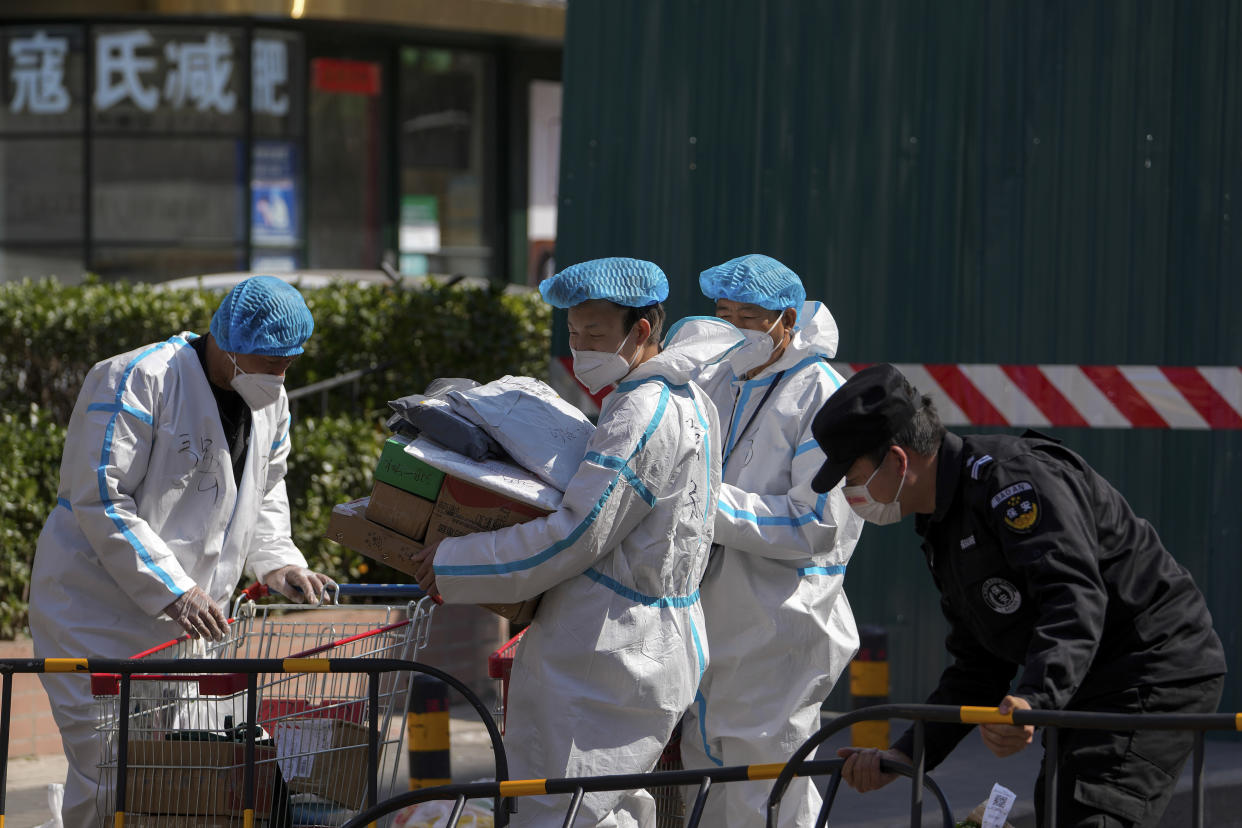 Security guards in protective gear load goods on a trolley to transfer to barricaded residential buildings locked down for health monitoring following a COVID-19 case detected in the area, Monday, March 28, 2022, in Beijing. China began its largest lockdown in two years Monday to conduct mass testing and control a growing outbreak in its largest city of Shanghai as questions are raised about the economic toll of the nation's "zero-COVID" strategy. (AP Photo/Andy Wong)