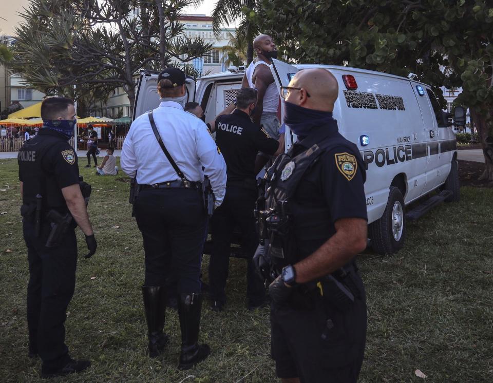 An unidentified man is detained and later arrested on Sunday, March 21, 2021, at 5th Street and Ocean Drive while crowds of Miami Beach spring-breakers walk Ocean Drive several hours prior to a city-wide curfew that was put into effect after several nights of mass arrests. An 8 p.m. curfew has been extended in Miami Beach after law enforcement worked to contain unruly crowds of spring break tourists (Carl Juste/Miami Herald via AP)