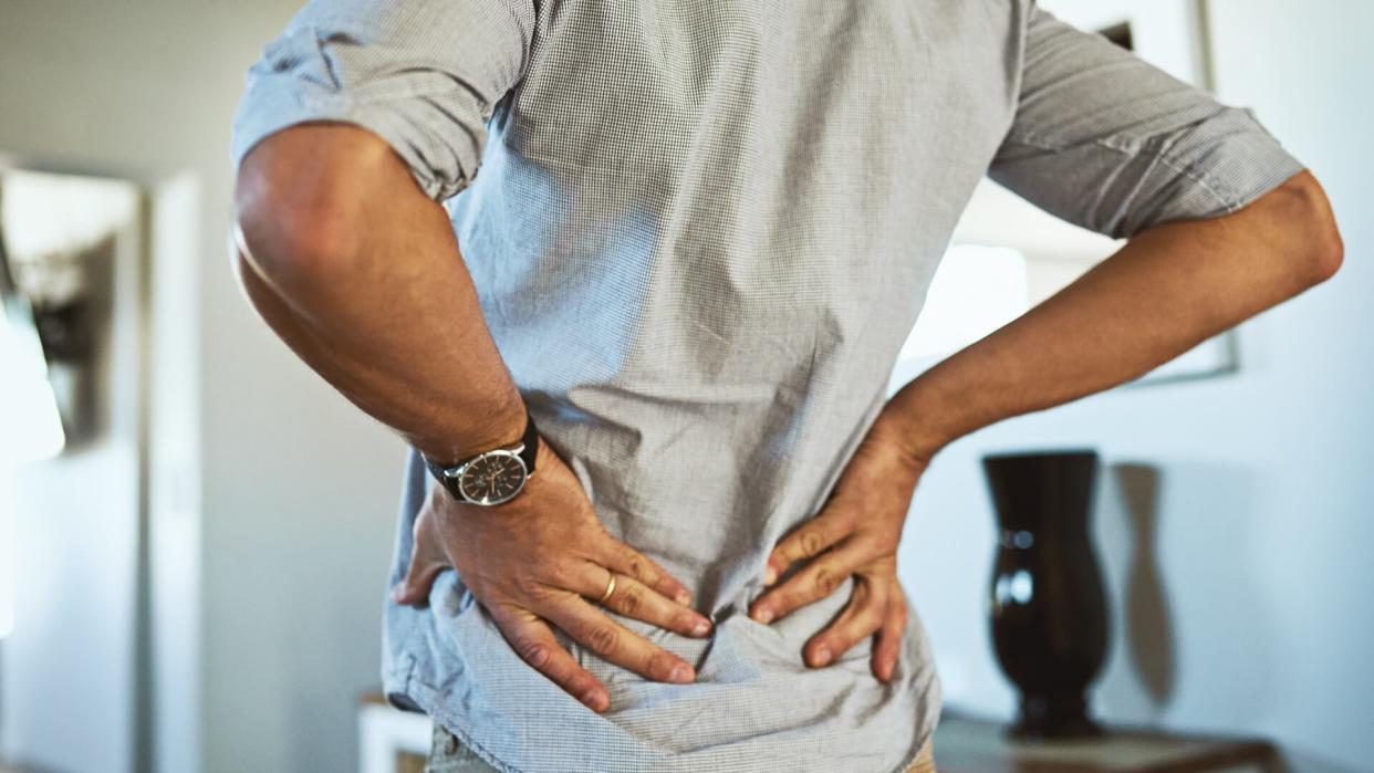 Rearview shot of an unrecognizable man holding his back in discomfort due to pain inside at home.