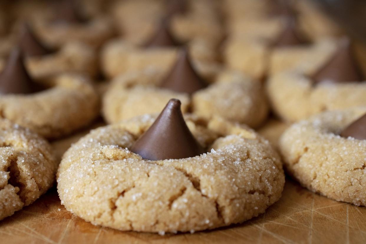 Peanut butter blossom cookies up close with rows of cookies behind on wooden cutting board.  Macro shot.