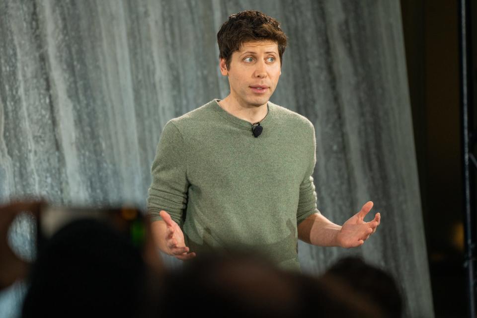 Sam Altman gesturing with both hands while talking to members of the media.