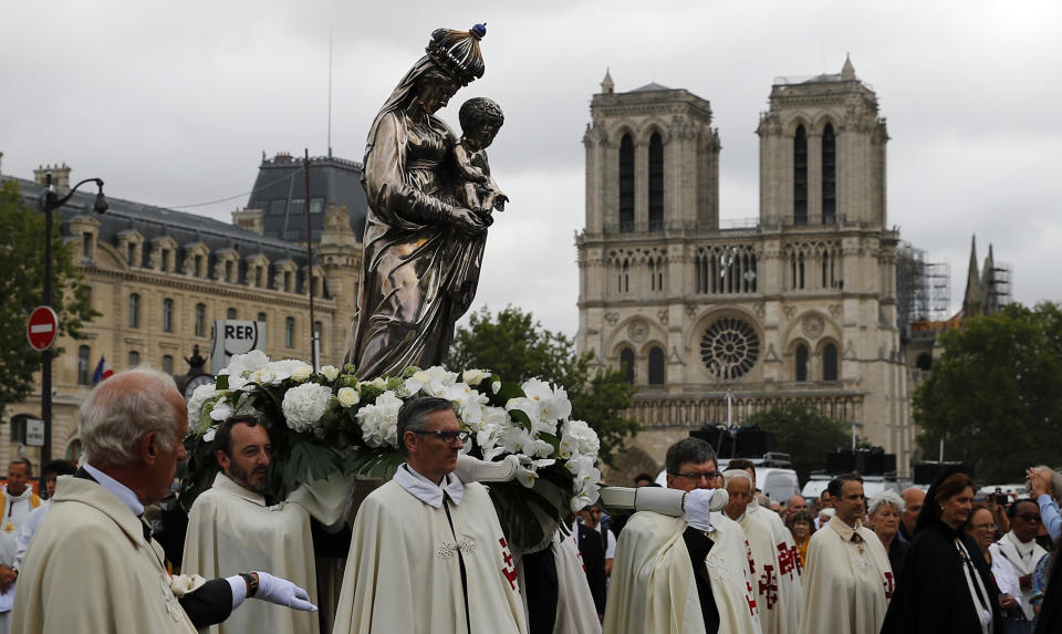 Catholic clergymen and pilgrims take part in an emotional procession with the statue of the Virgin Mary rescued from the April blaze past the fire-ravaged Notre Dame Cathedral to celebrate the Assumption of the Virgin in Paris, Thursday, Aug. 15, 2019. (AP Photo/Francois Mori)