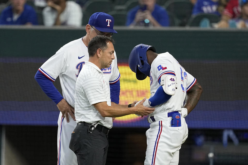 Texas Rangers head athletic trainer Matt Lucero, left, and manager Bruce Bochy, left rear, attend to Adolis Garcia, right, after Garcia was hit by a pitch in the eighth inning of a baseball game against the Tampa Bay Rays, Wednesday, July 19, 2023, in Arlington, Texas. Garcia left the game with an unknown left arm injury. (AP Photo/Tony Gutierrez)