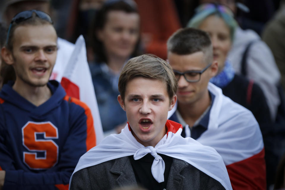 Belarusian opposition supporters cover themselves by old Belarusian national flag gather at Independence Square in Minsk, Belarus, Wednesday, Aug. 26, 2020. Protests demanding the resignation of Belarus' authoritarian President Alexander Lukashenko have entered their 18th straight day on Wednesday. (AP Photo/Sergei Grits)