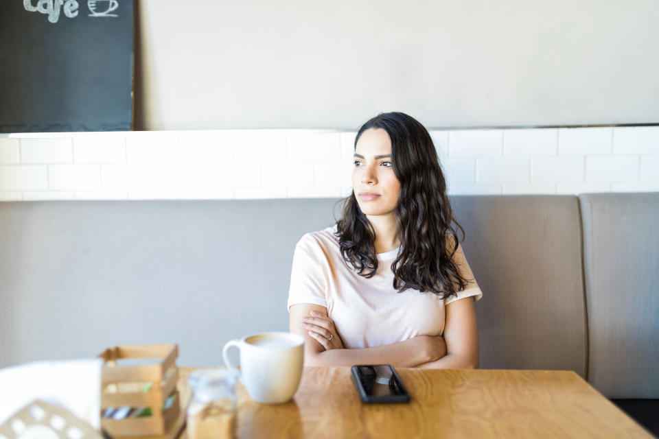 Angry young woman with arms crossed waiting for her date in cafe