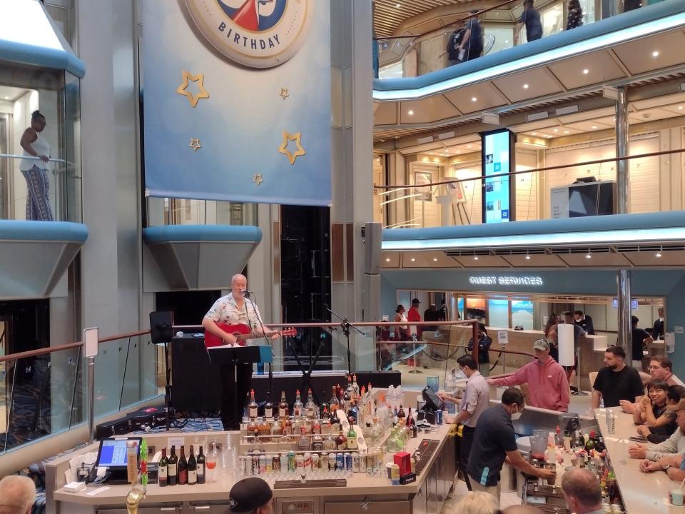 Shot of a man playing a red guitar in front of a crowd on a Carnival Radiance cruise ship