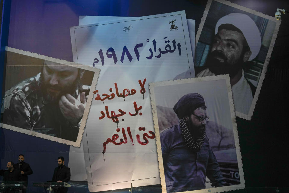 Musicians play under pictures of slain Hezbollah leaders -- Hezbollah military commander Imad Mughniyeh, left, Hezbollah leader Sheik Ragheb Harb, right, and Sheik Abbas Musawi, center, -- during an annual ceremony commemorating the killing of some of the Iran-backed group's top political and military leaders, in the southern suburb of Beirut, Lebanon, Wednesday, Feb. 16, 2022. Hezbollah leader Sheik Hassan Nasrallah revealed Wednesday in a televised speech that his militant faction has been manufacturing military drones in Lebanon and has the technology to turn thousands of missiles in their possession into precision-guided munitions. Arabic reads, "Decision was made in 1982. No reconciliation but holy war until victory is achieved." (AP Photo/Hassan Ammar)