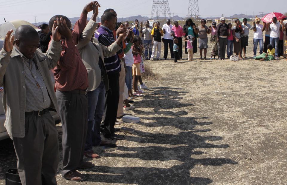 A group of churchgoers join hand in prayer at the site, Sunday Aug. 19, 2012 at the Lonmin platinum mine near Rustenburg, South Africa, during a memorial service for 34 dead striking miners who were shot and killed bt police last Thursday. Miners must return to work Monday or face being fired from the mine where rivalry between unions has exploded into violence. (AP Photo/Denis Farrell)