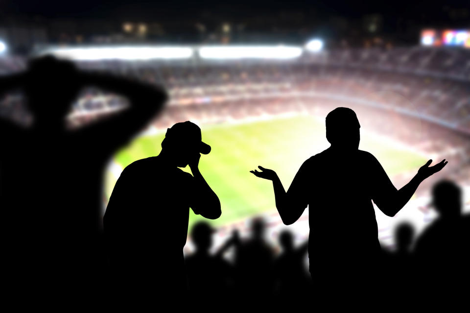Silhouettes of fans making upset gestures in a sports stadium.