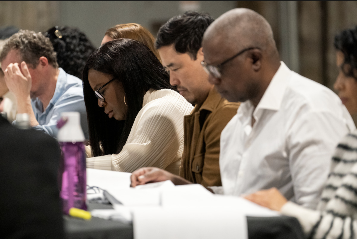 Uzo Aduba sits at a table among others looking at papers in front of them.