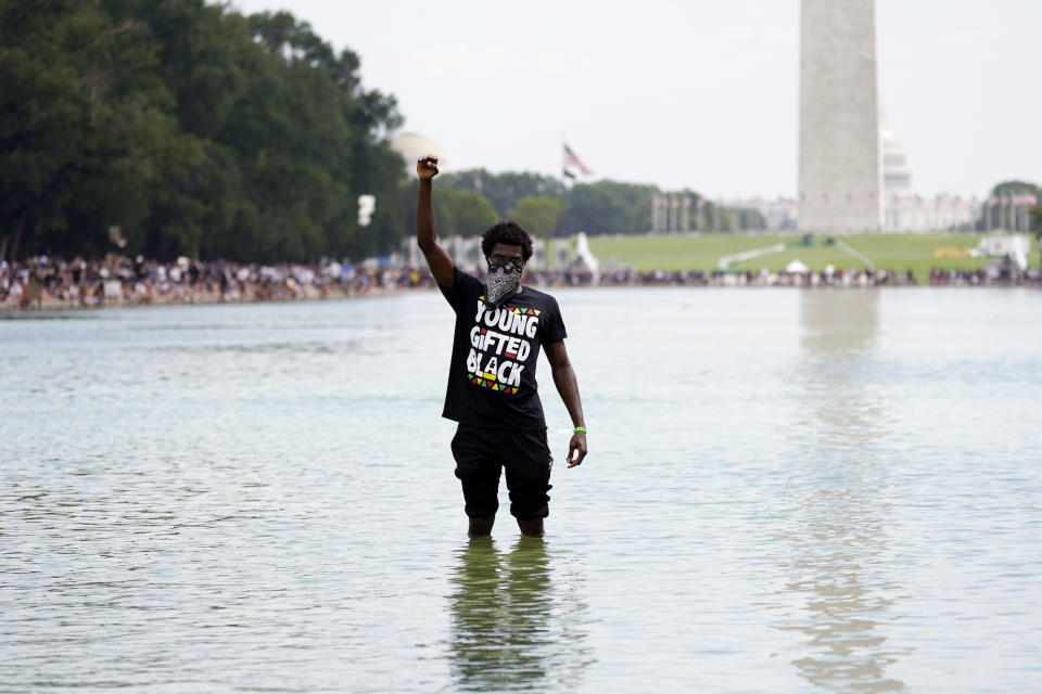 A man stands in the Reflecting Pool as people attend the March on Washington, Friday Aug. 28, 2020, in Washington, on the 57th anniversary of the Rev. Martin Luther King Jr.'s "I Have A Dream" speech. (AP Photo/Carolyn Kaster)