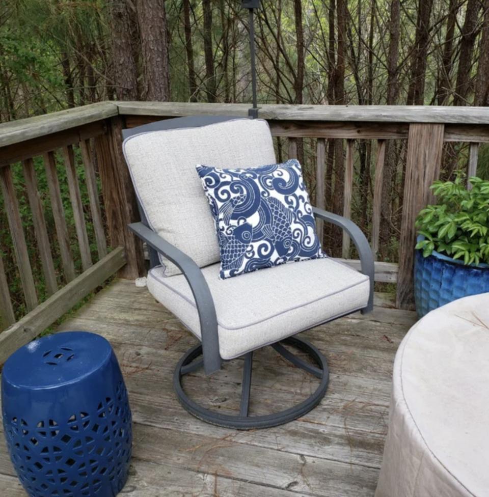 Outdoor patio chair with a decorative pillow, positioned next to the blue ceramic stool
