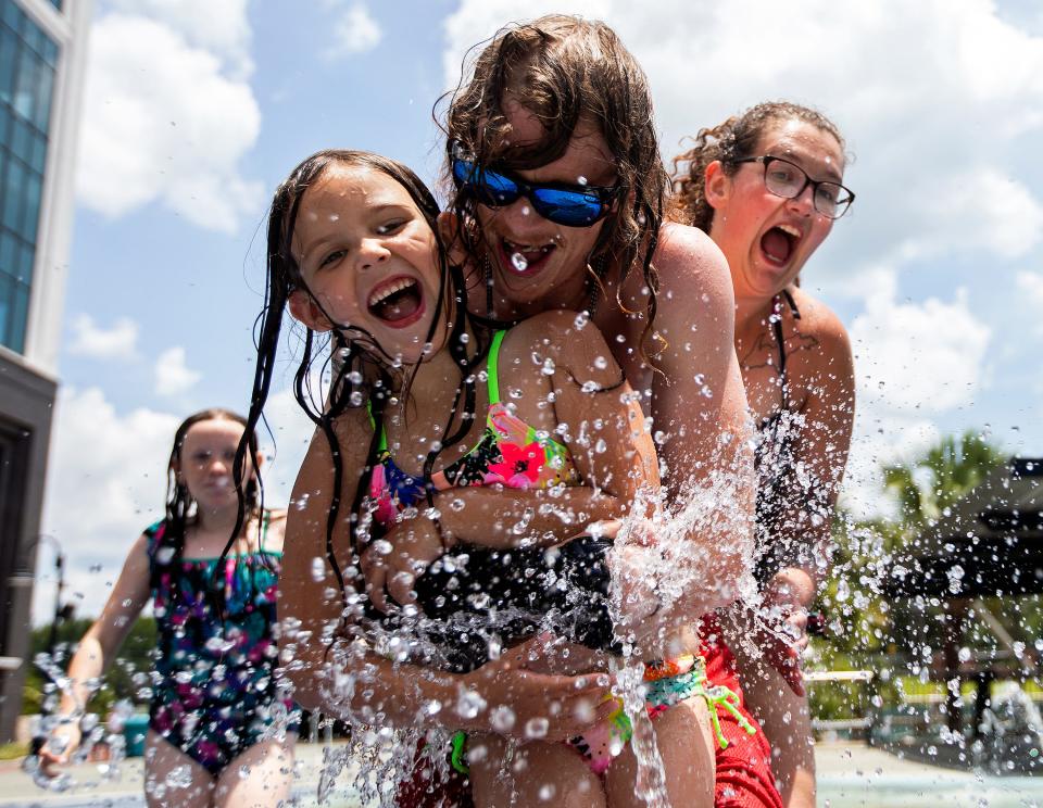 James McNeely holds his daughter, Madison McNeely, as the two play in a splash pad at Imagination Fountain in Cascades Park in Tallahassee, Fla. on Tuesday, Jun 21, 2022, the official first day of summer. McNeely's other daughter, Abby, and his fiance Olivia Koenig, run up to join the pair.