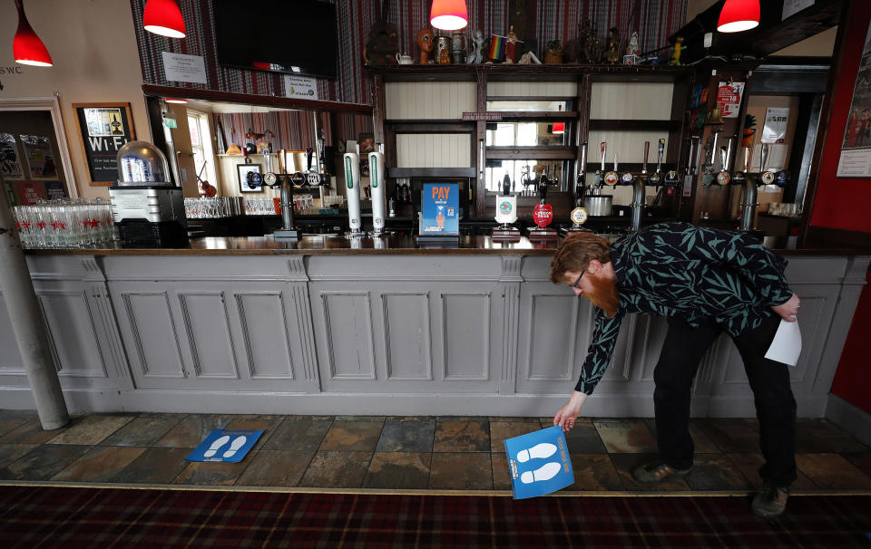 Image: Owner Are Kjetil Kolltveit from Norway places markers for social distancing on the front of the bar at the Chandos Arms pub in London (Frank Augstein / AP)