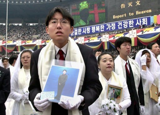 File photo taken in 2000 shows newly weds, some holding portraits of partners who couldn't attend, listening to Unification Church founder Sun Myung Moon preach during a mass wedding ceremony in Seoul. The church claims a worldwide following of three million