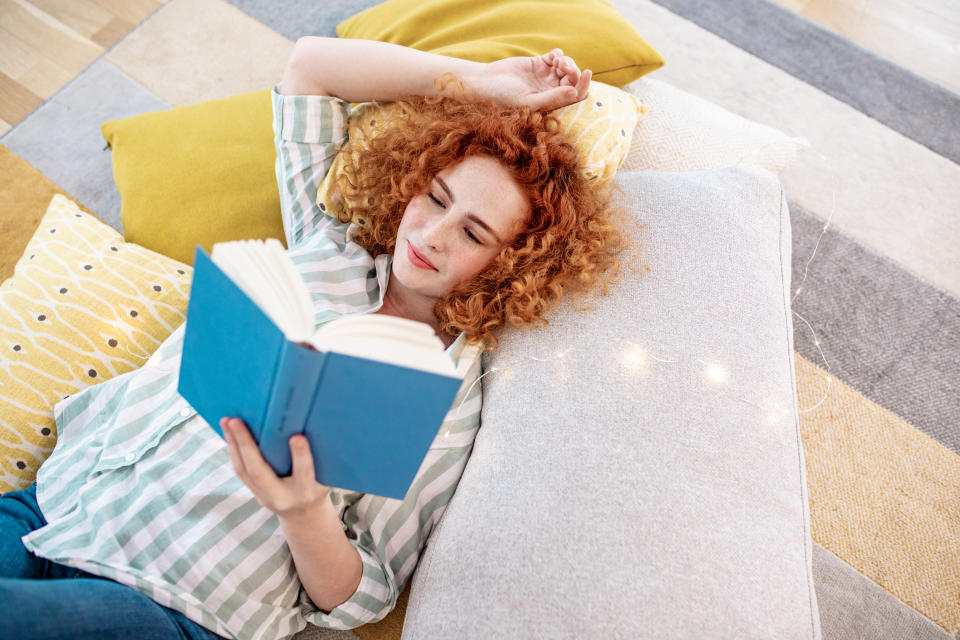 A young woman is on the floor at home, she is reading a book and enjoying