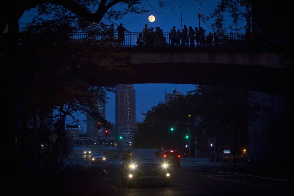 People stand and look at the moon one day ahead of the Supermoon phenomenon from a bridge over 42nd St. in the Manhattan borough of New York July 11, 2014. Occurring when a full moon or new moon coincides with the closest approach the moon makes to the Earth, the Supermoon results in a larger-than-usual appearance of the lunar disk. REUTERS/Carlo Allegri (UNITED STATES - Tags: SOCIETY CITYSCAPE)