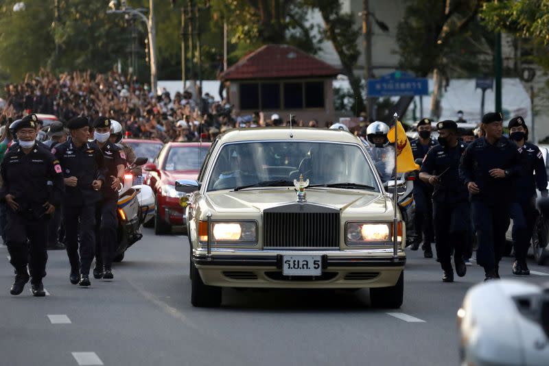 The royal motorcade carrying Thailand's Queen Suthida and Prince Dipangkorn drives past a group of anti-government demonstrators in front of Government House in Bangkok