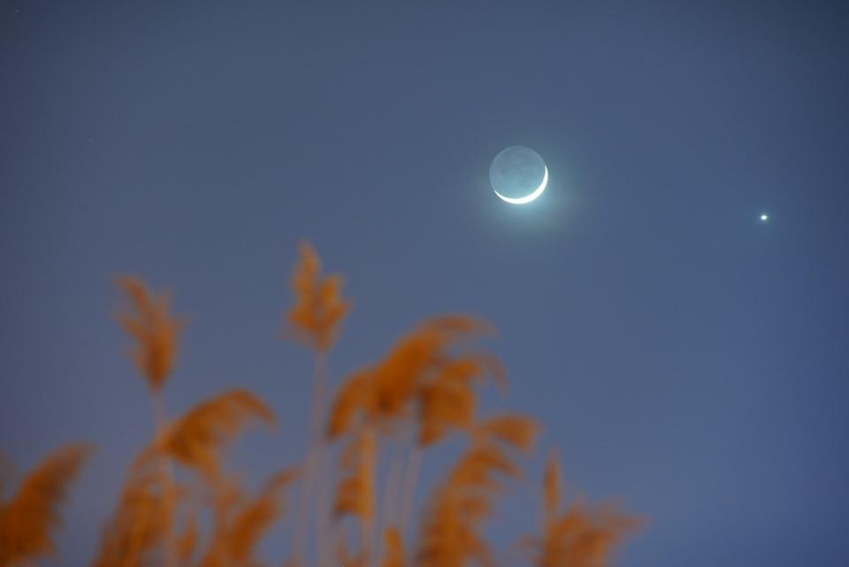 eine dünne Mondsichel am Himmel mit einer leuchtenden Kugel daneben