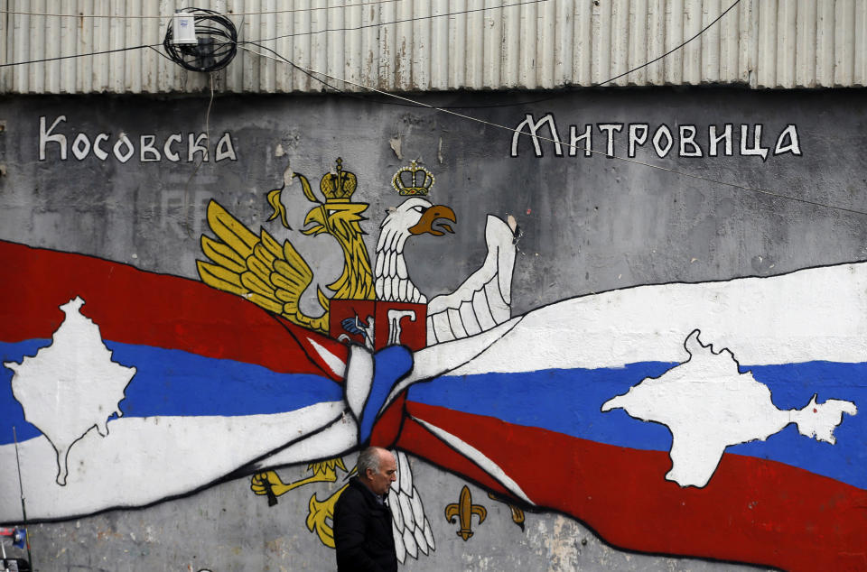 A man walks by graffiti that shows Serbian, left, and Russian flags with maps of Kosovo and Crimea in northern, Serb-dominated part of ethnically divided town of Mitrovica, Kosovo, Saturday, Dec. 15, 2018. Serbia threatened a possible armed intervention in Kosovo after the Kosovo parliament on Friday overwhelmingly approved the formation of an army. Russia denounced the move to form a Kosovo army, saying the ethnic Albanian force must be "disbanded" by NATO in Kosovo. (AP Photo/Darko Vojinovic)