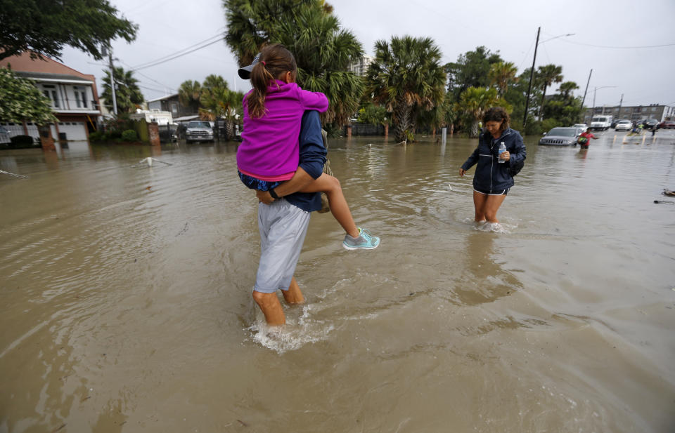 FILE - In this June 21, 2017 file photo, Don Noel carries his daughter Alexis, 8, with his wife Lauren, right as they walk through a flooded roadway to check on their boat in the West End section of New Orleans. The Southern tourist destination is grappling with longstanding infrastructure challenges, including potholes, drainage problems and sporadic drinking water issues. (AP Photo/Gerald Herbert, File)