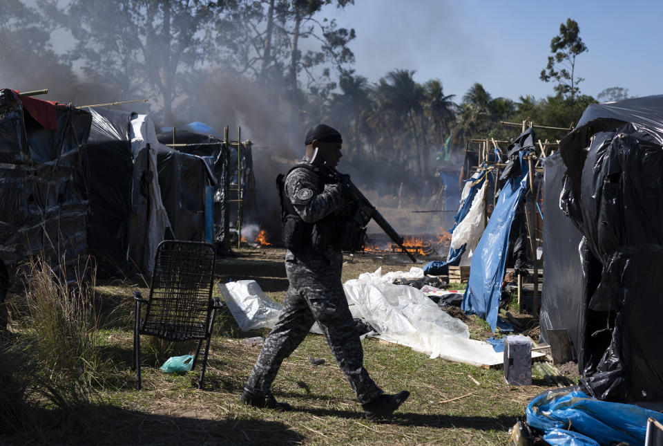 A police officer walks through the settlement coined the "First of May Refugee Camp," named for the date people moved on the land designated for a Petrobras refinery, in Itaguai, Rio de Janeiro state, Brazil, Thursday, July 1, 2021, amid the new coronavirus pandemic. (AP Photo/Silvia Izquierdo)