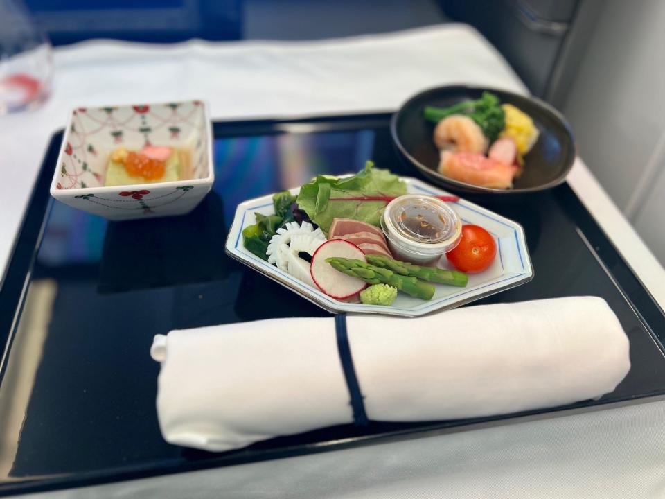 Three dishes with seafood on a tray with silverware wrapped in a napkin.