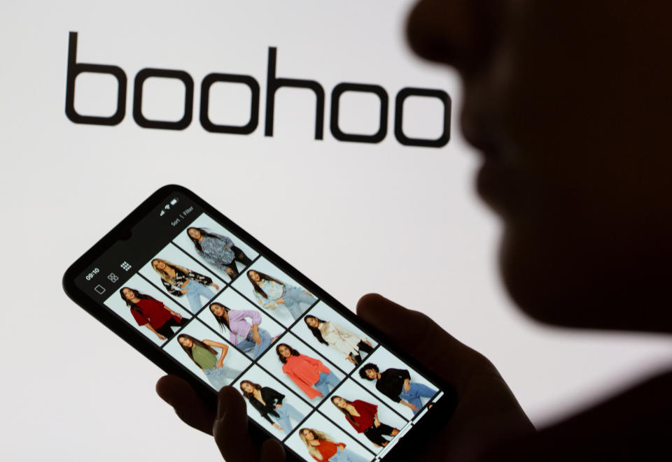 A woman poses with a smartphone showing the Boohoo app in front of the Boohoo logo on display in this illustration taken September 30, 2020. REUTERS/Dado Ruvic/Illustration