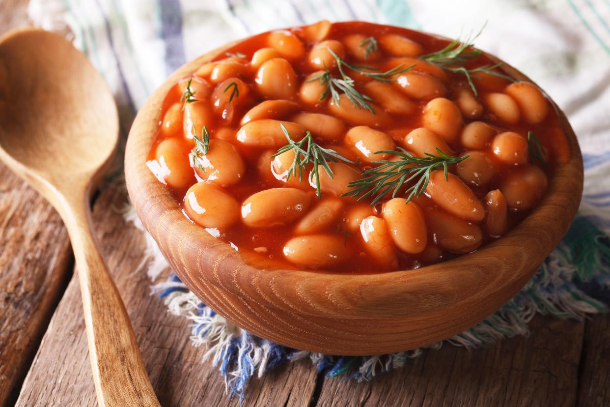 Instant pot baked beans in a wooden bowl with a wooden spoon next to it, on a blue and white napkin on a rustic wooden table