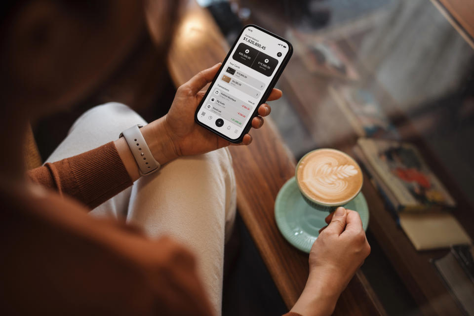 A person is holding a smartphone with a financial app open, displaying transaction details, while also holding a latte in a green cup