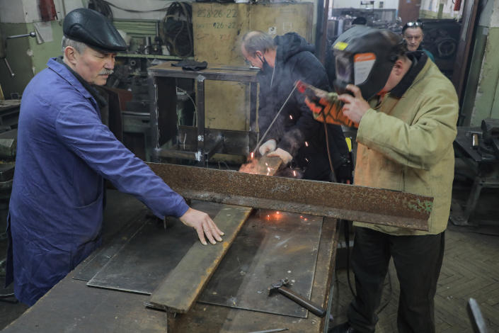 Four men in a workshop as one welds roughly four-feet-long steel beams together to form a cross.