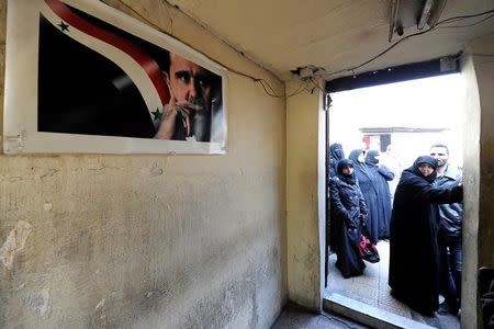 Civilians wait outside a government military police centre to visit their relatives, who were evacuated from the eastern districts of Aleppo and are being prepared to begin their military service, in Aleppo, Syria December 11, 2016. A poster depicting Syria's President Bashar al-Assad is seen inside a room. REUTERS/Omar Sanadiki