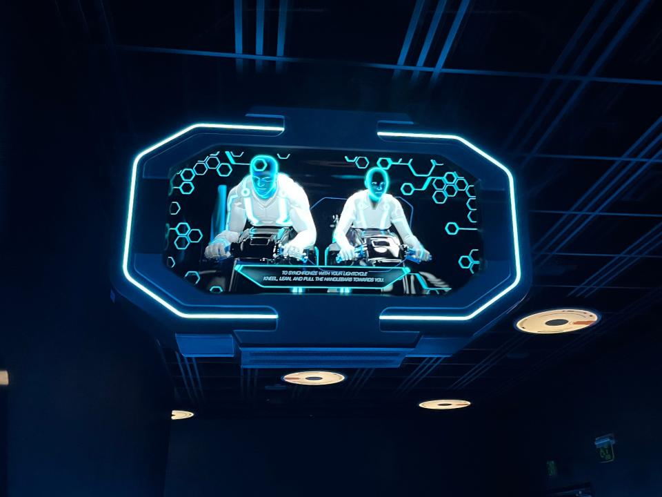 screen showing people riding on the lightcycles on tron coaster at magic kingdom