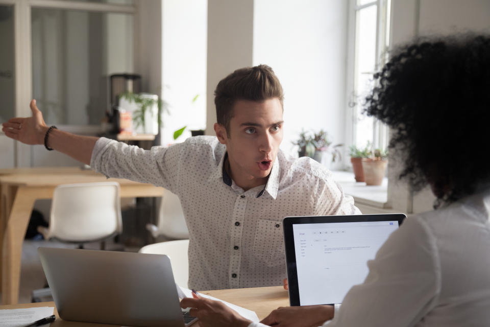 A man with expressive gestures argues with a woman working on a laptop in an office setting