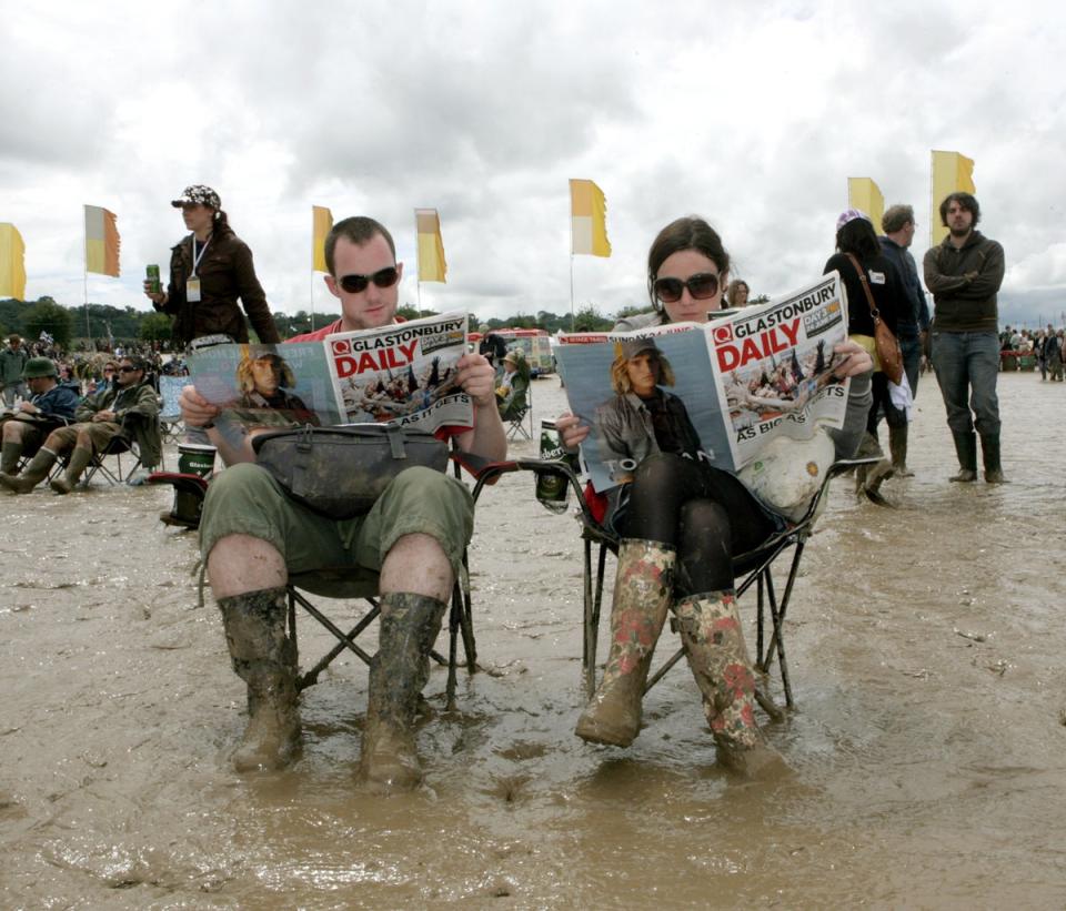 A couple read the free paper at a previous wet Glastonbury Festival at Worthy Farm in Pilton, Somerset (Anthony Devlin/PA) (PA Archive)