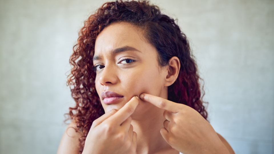 woman in mirror squeezing a pimple