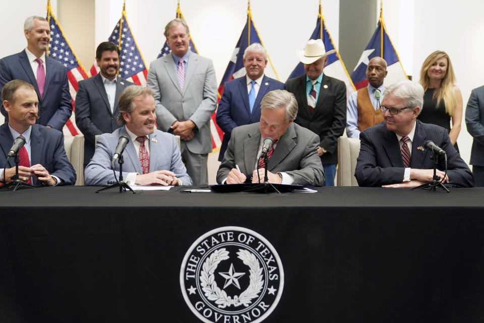 Texas Gov Greg Abbott signs Senate Bill 1, also known as the election integrity bill, into law with State Sen. Bryan Hughes, R-Mineola, front center left, Andrew Murr, R-Junction, front left, and Lieutenant Governor Dan Patrick, front right looking on with others in the back ground in Tyler, Texas, Tuesday, Sept. 7, 2021. (AP Photo/LM Otero)