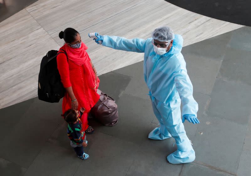 A health worker in personal protective equipment (PPE) checks the temperature of a passenger at a railway station, amid the spread of the coronavirus disease (COVID-19), in Mumbai