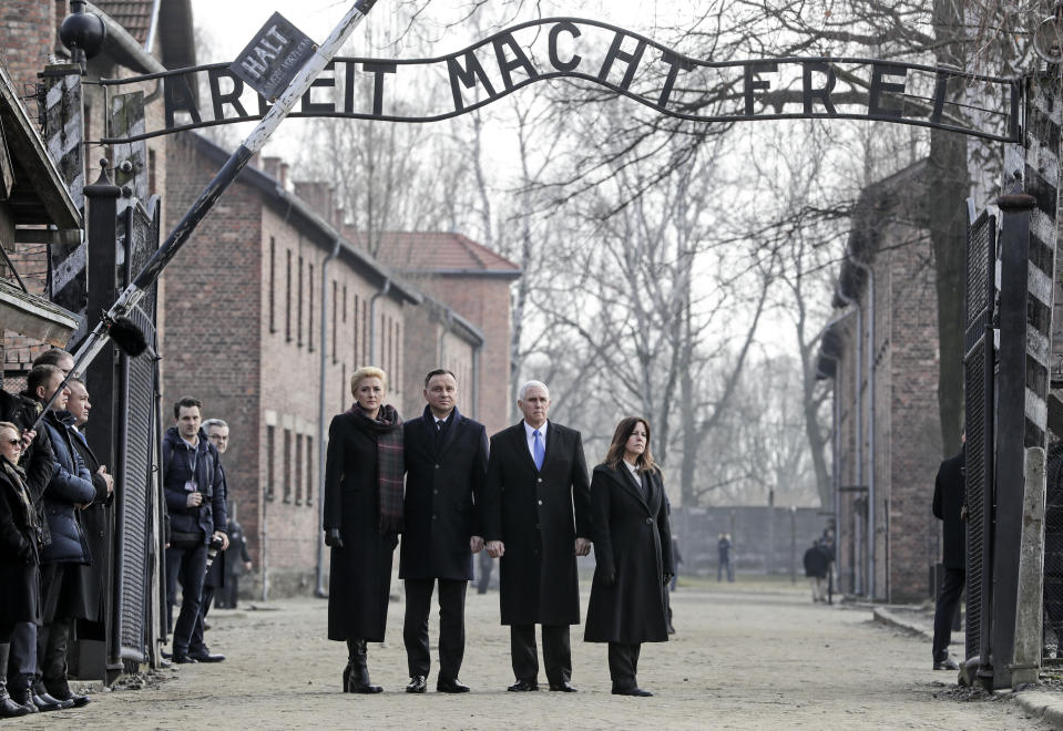 United States Vice President Mike Pence and his wife Karen Pence, right, stand with Poland's President Andrzej Duda and his wife Agata Kornhauser-Duda, left, under the gate during their visit at the Nazi concentration camp Auschwitz-Birkenau in Oswiecim, Poland, Friday, Feb. 15, 2019. The sign over the gate reads 'work makes one free'. (AP Photo/Michael Sohn)