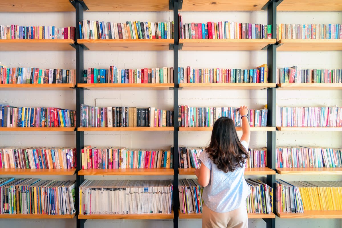 A person takes book from a bookshelf inside a library. 