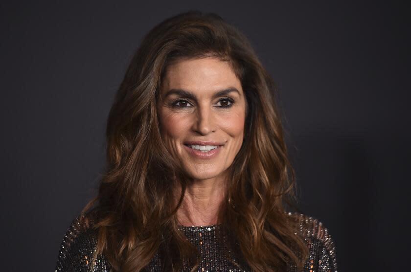 Cindy Crawford smiling against a dark background wearing a sparkling dress