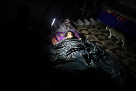 A disabled Palestinian woman lies on a mattress, as her relative holds a torch to show her to the photographer during a power cut in Khan Younis in the southern Gaza Strip, July 3, 2017. REUTERS/Mohammed Salem