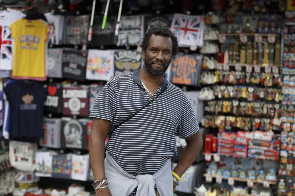 Paul Tomo poses for a photo in front of a souvenir stand in Westminster in London, Wednesday, July 22, 2020. "Two things, if we really needed them why weren't they introduced in the beginning. They gave a deadline before they implemented it which gives you a clear indication to question what you are being told because its clearly for control purposes not for your protection whatsoever." (AP Photo/Kirsty Wigglesworth)