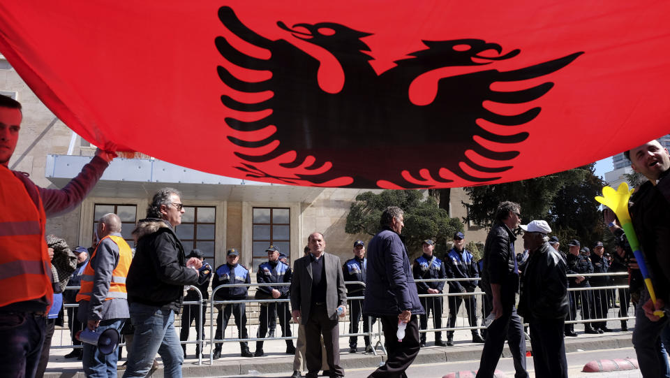 Protesters hold an Albanian flag during an anti-government rally in Tirana, Albania, Saturday, March 16, 2019. Thousands of supporters of the center-right Democratic Party-led opposition have gathered on Saturday in front of Socialist Party's Prime Minister Edi Rama to demand his resignation, a transitory Cabinet without him that will prepare fresh elections. (AP Photo/Hektor Pustina)