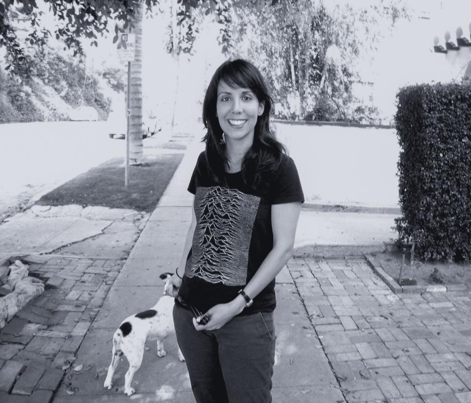 A woman stands with a little dog in the background