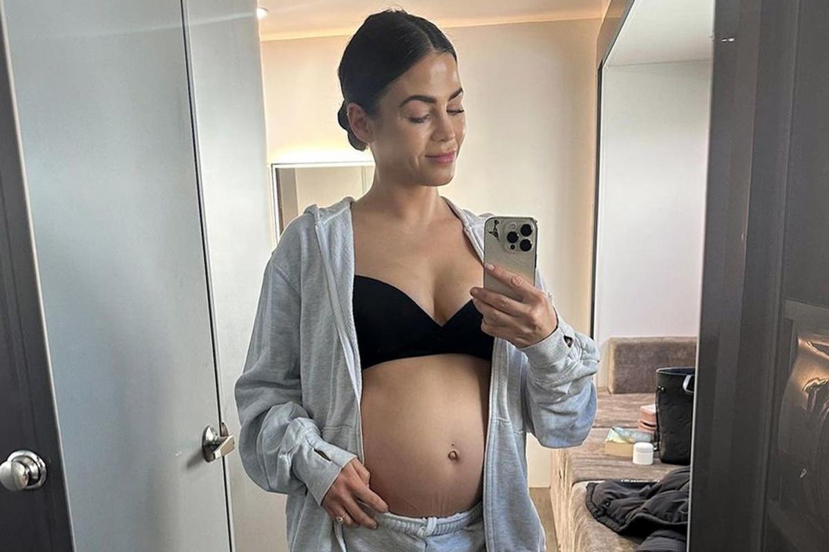 Pregnant woman in sports bra using smart phone in doorway at home